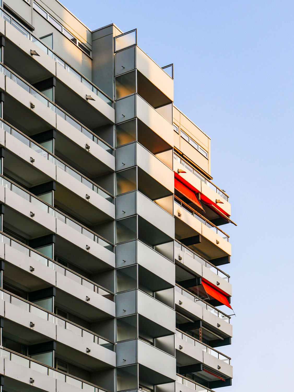 View of the facade of a high-rise building with many balconies. Some of the balconies have a red awning.