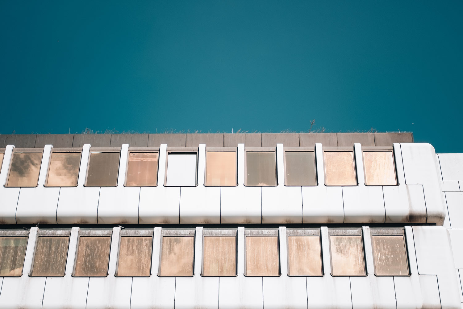 {:gb}Facade of a white building, the windows of which are mirrored in copper color.{:}{:de}Fassade eines weißen Gebäudes, dessen Fenster kupferfarben verspiegelt sind.{:}