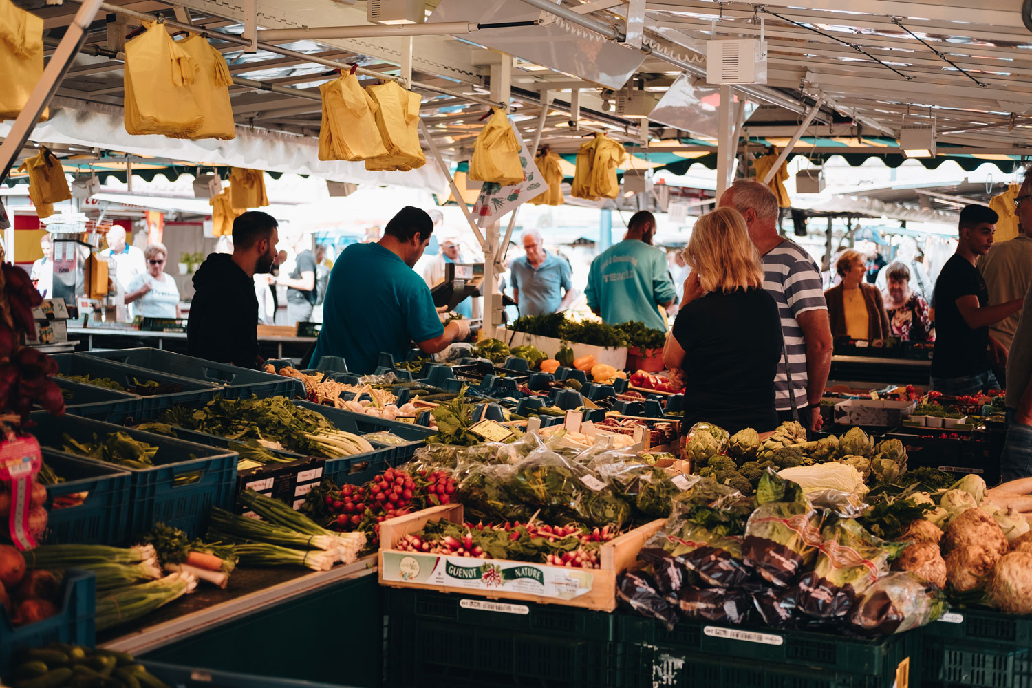 A fruit and vegetable stand in a busy market. An employee weighs a bag.