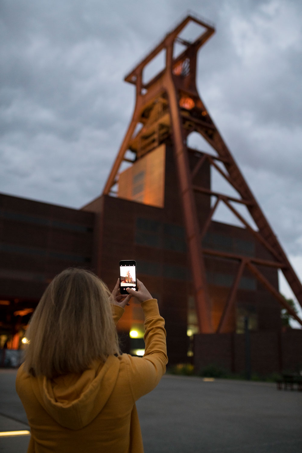 Eine Frau mit Smartphone fotografiert den Förderturm des Deutschen Bergbau-Museums in Bochum bei Sonnenuntergang.
