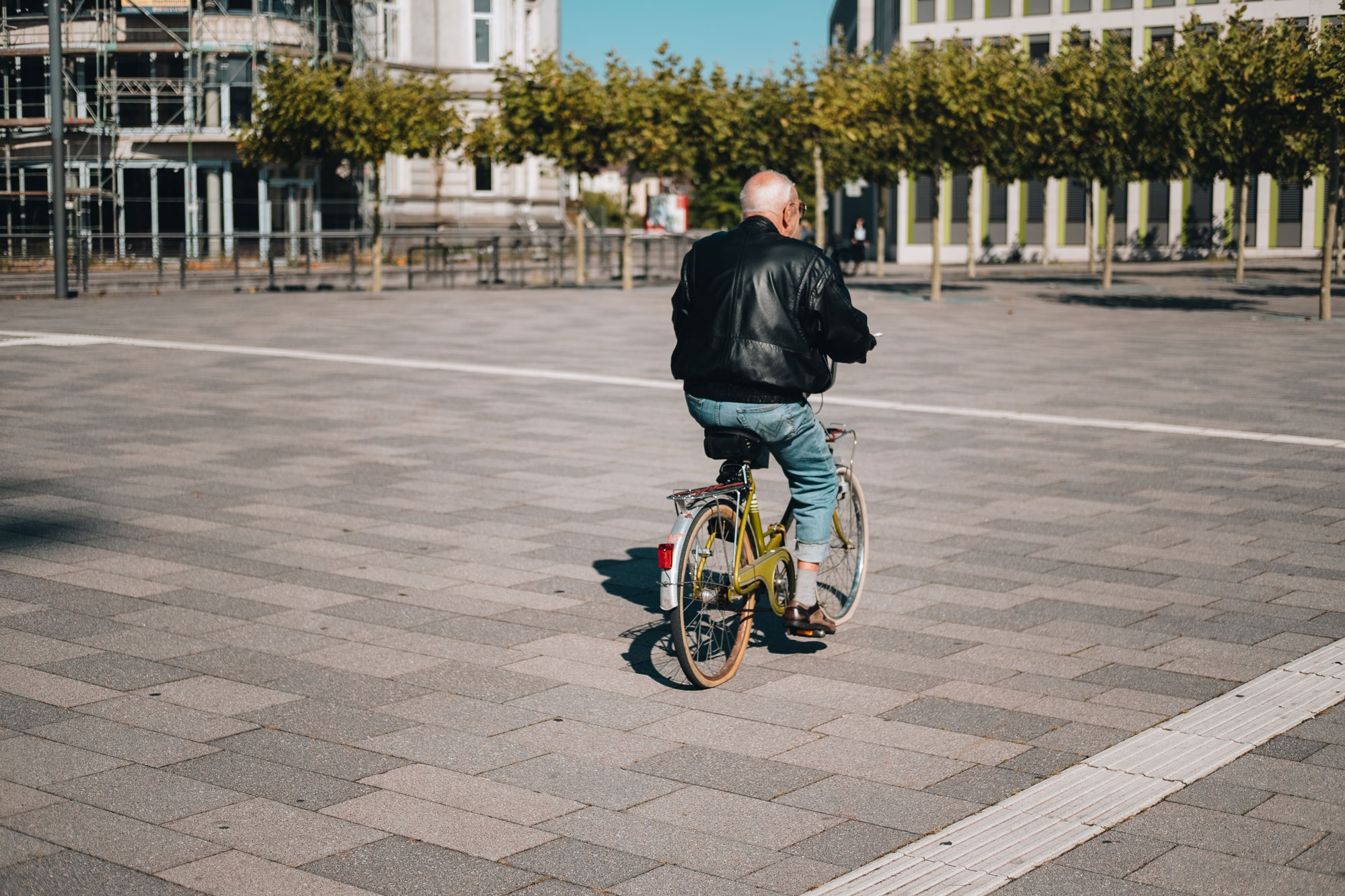 An elderly man on a yellow bicycle rides an asphalt square.