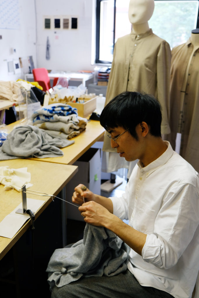 {:gb}Hiroyuki Murase, founder and designer of the "Suzusan" label is sitting at a table and knotting a thread.{:}{:de}Hiroyuki Murase, Gründer und Designer des Labels "Suzusan" sitzt an einem Tisch und verknotet einen Faden.{:}