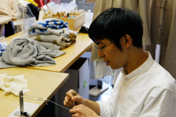 Hiroyuki Murase, founder and designer of the "Suzusan" label is sitting at a table and knotting a thread.