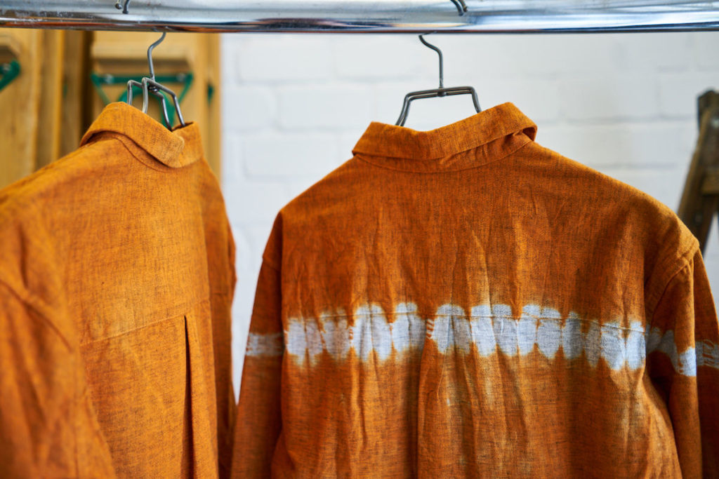 Orange shirts of the label "Suzusan" hang on a stand.